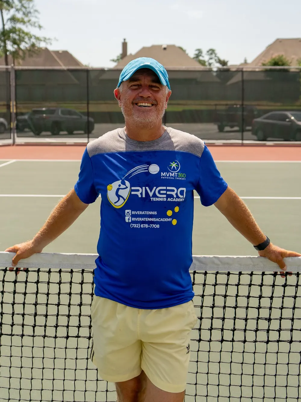 Alfredo Rivera, Director and Owner of Rivera Tennis Academy, standing at the net on an outdoor hard court.