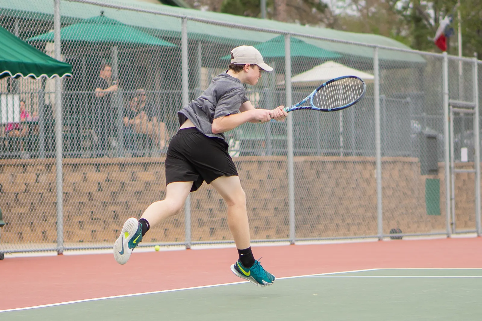 Player airborne mid-rally, both feet off the ground and racquet extended, on an outdoor hard court.