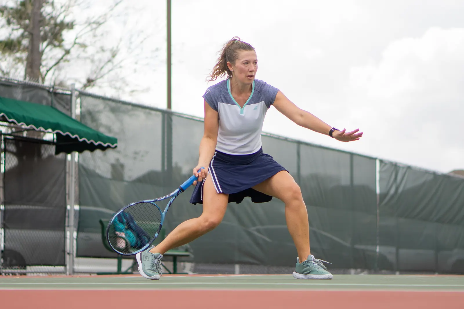 Player lunging in a wide low stance with the racquet drawn back for a forehand, ball airborne.