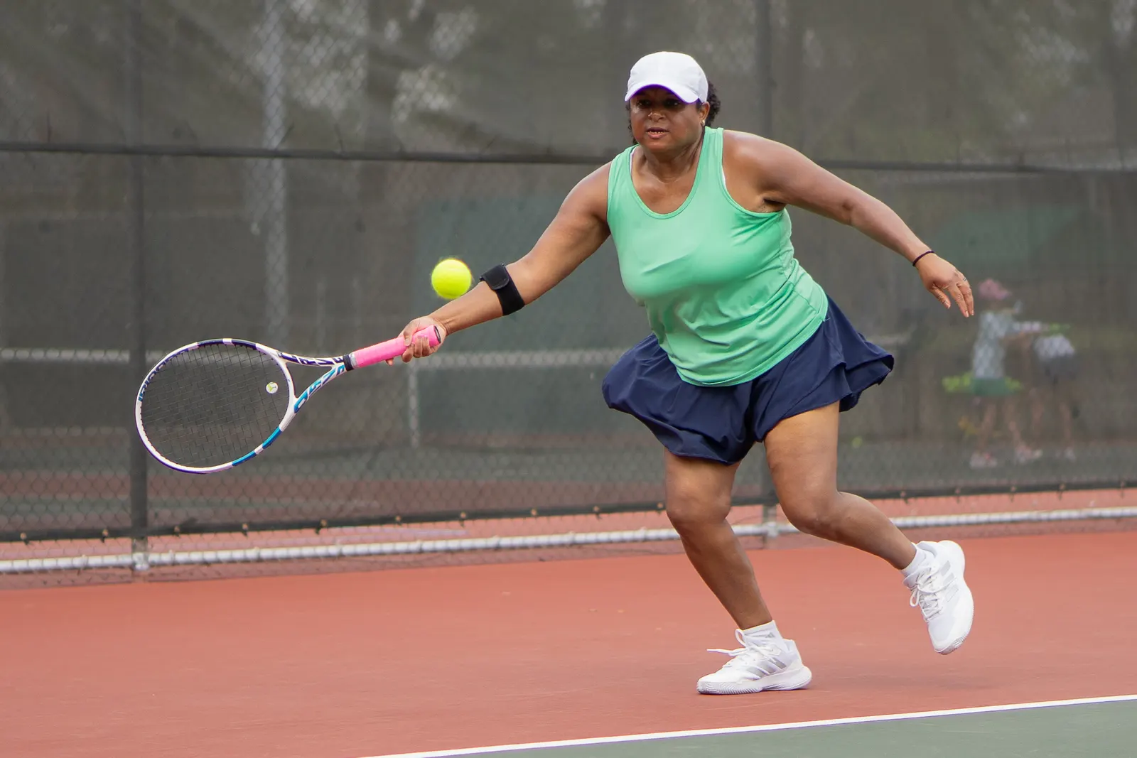 Player stretching wide to reach a low forehand, ball just above the strings, on an outdoor hard court.