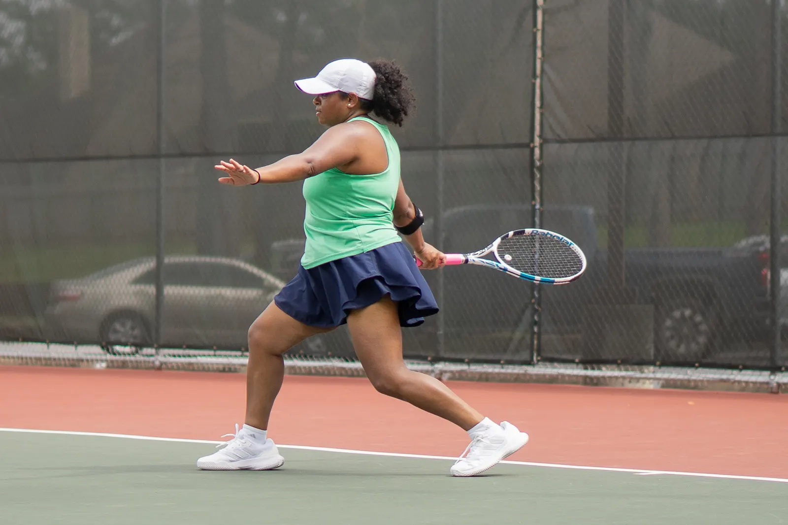 Woman taking the racquet back for a forehand on an outdoor hard court, ball in the air to her left.