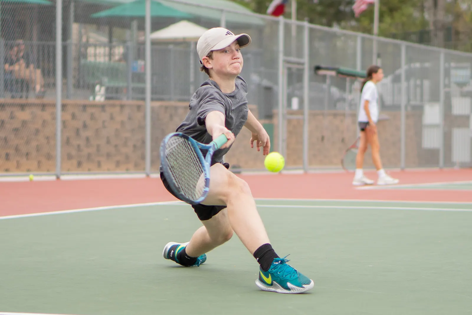 Player sliding into a deep lunge to reach a low forehand, ball in the air beside the racquet.