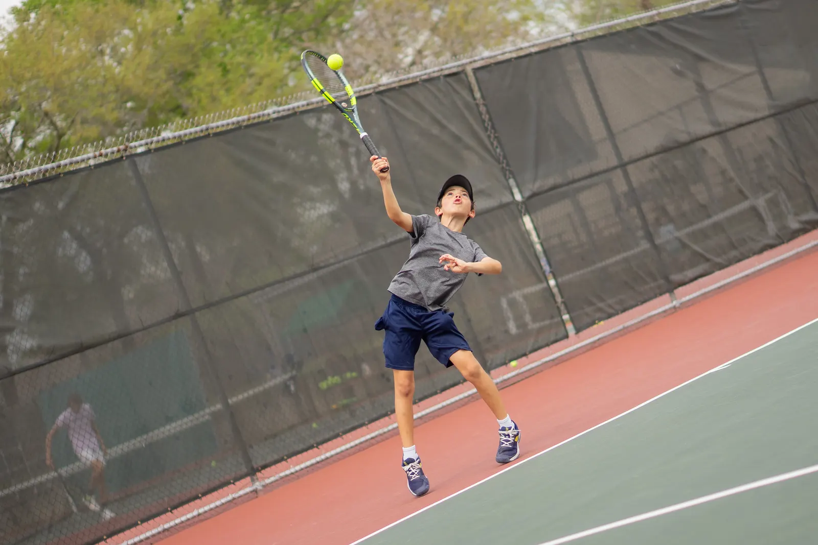 Young player jumping to strike a ball above their head with the racquet at full extension.